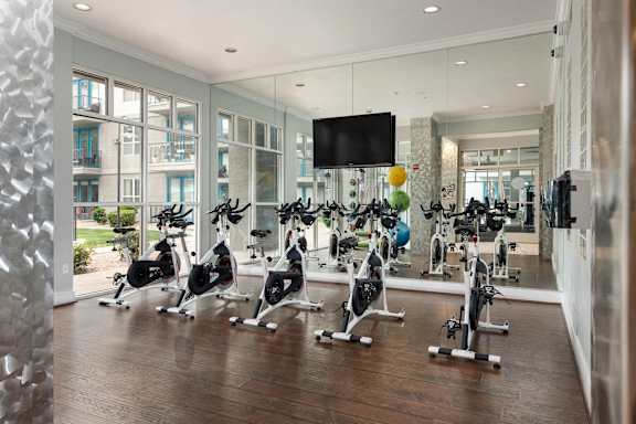 A gym with a row of stationary bikes and a television mounted on the wall.