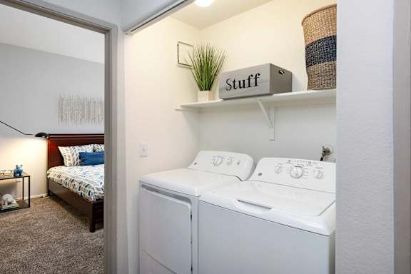 A small bedroom with a bed, a washing machine, and a shelf with a box labeled "Stuff".