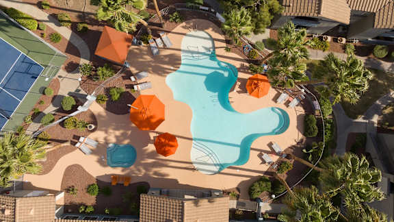 An aerial view of a pool and a tennis court surrounded by palm trees.