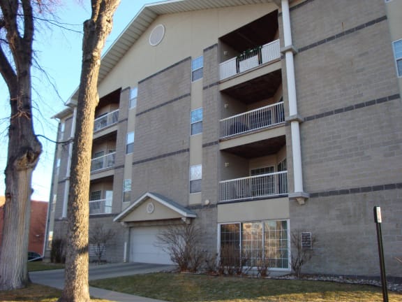 an apartment building with a garage and a tree in the foreground at Park Ridge Apartments, North Dakota