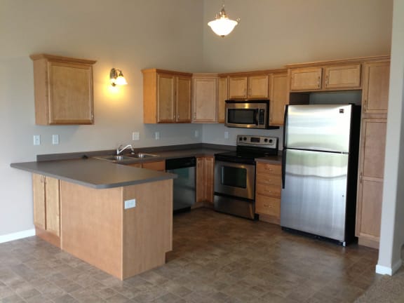 a kitchen with wooden cabinets and stainless steel appliances at The Pines Townhomes, North Dakota