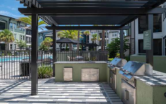 A patio area with a grill and a pool in the background.