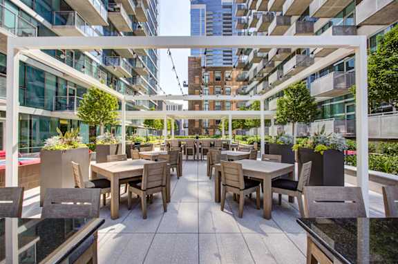 A patio with tables and chairs is surrounded by buildings.