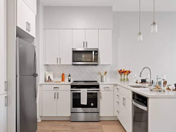 A modern kitchen with a refrigerator on the left and a stainless steel oven in the center.