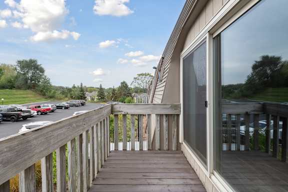 A wooden deck with a railing and a glass door leading to a house.