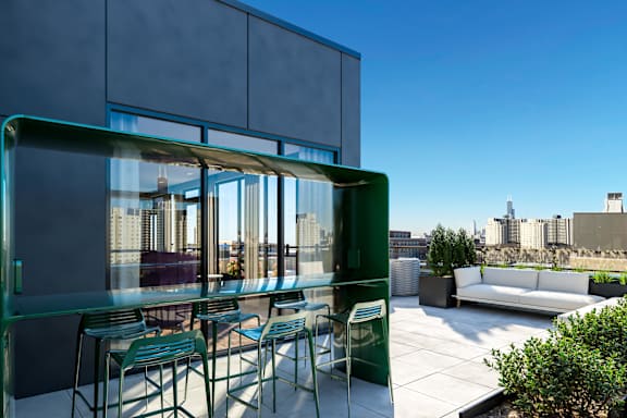 A glass table with chairs is on a patio with a view of the city.