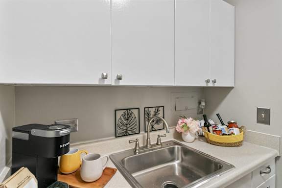 A kitchen with a sink, a coffee maker, and a basket of fruit.