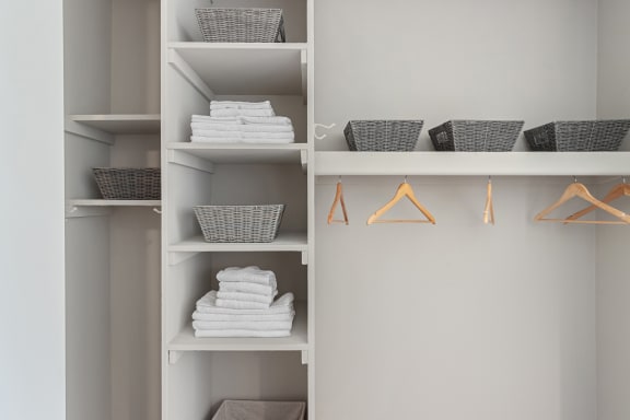a white shelving unit with baskets and hangers and folded white towels at The Pavilion, Detroit, MI, 48207