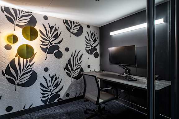 A modern office with a leaf patterned wallpaper and a desk with a computer.