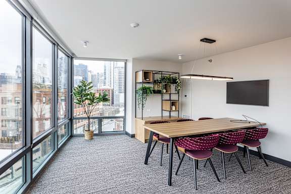 A conference room with a long table and chairs, a TV on the wall, and a view of the city outside the windows.