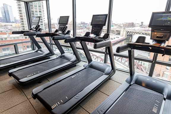 Three treadmills are lined up in a row in a gym with a city view.