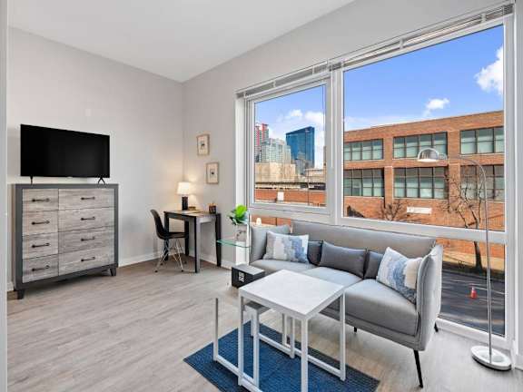 A living room with a grey couch, a white coffee table, and a large window overlooking a cityscape.