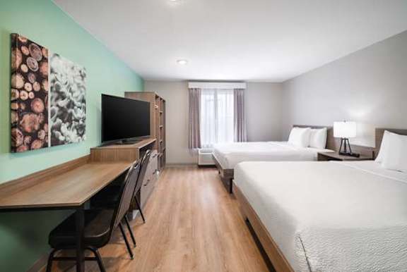 A hotel room with two beds, a desk, and a television.