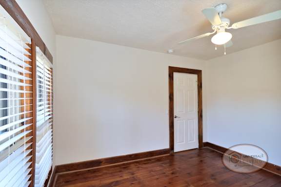A bedroom with hardwood floors, ceiling fan, and large window.