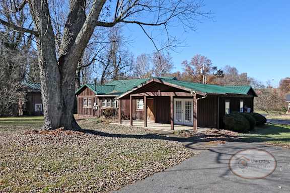 A rustic two bedroom cabin style home with green roof and paved driveway.