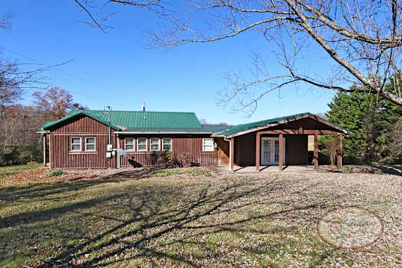 The front of a rustic two bedroom cabin style home with green roof and paved driveway.