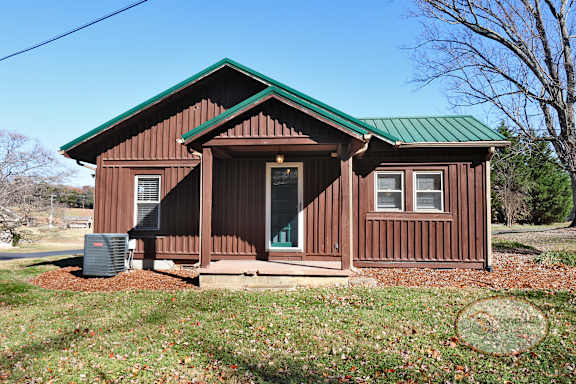 Side door to a rustic cabin style two bedroom home with a green roof.