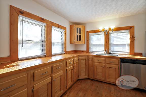 A kitchen with large windows, wooden cabinets and a stainless steel dishwasher.