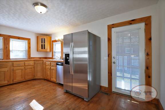 A kitchen with a stainless steel refrigerator, wooden cabinets, and hardwood flooring.