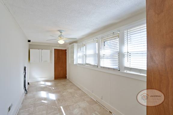 The large laundry room with white walls, vinyl flooring, ceiling fan, and a row of large windows.