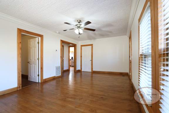 Living room with ceiling fan, hardwood flooring, and several doors.