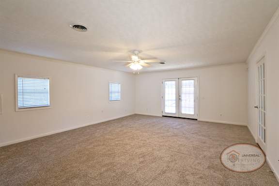 A spacious master bedroom with glass patio doors, carpet, and ceiling fan.