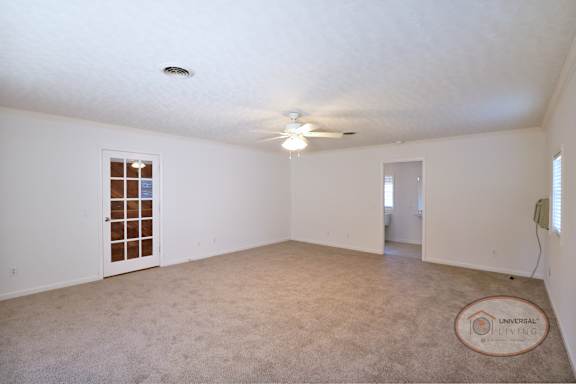 A spacious master bedroom with carpet, a glass door, and ceiling fan.