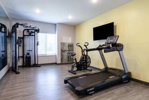 A treadmill with the brand name "SPRINT" on it is in the foreground of a well-equipped gym.
