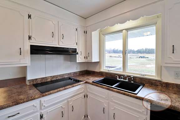 A kitchen with white cabinets and black cooktop.