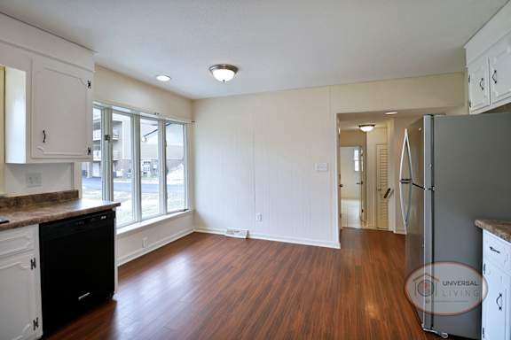 A kitchen with white cabinets, a large wall of windows, and hardwood floors.