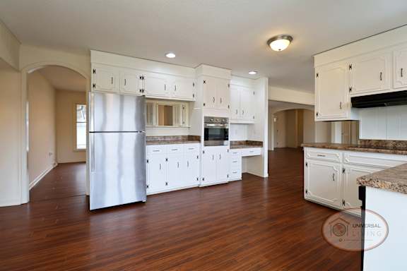 A kitchen with white cabinets, hardwood floors, and stainless steel refrigerator.
