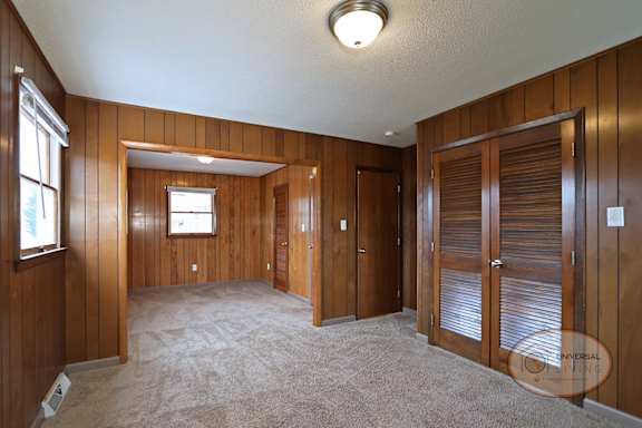 A room with wood paneling, closet, and catpet.