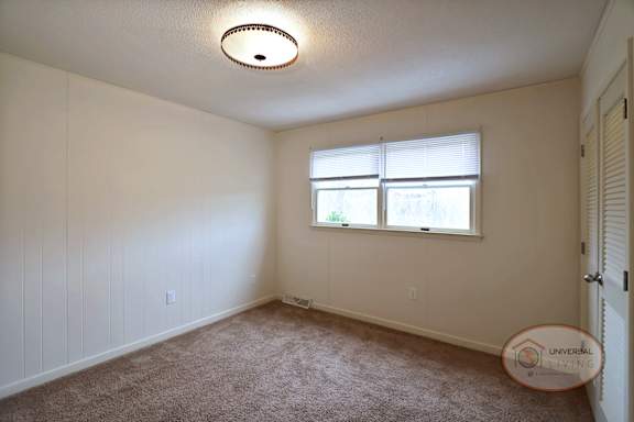 A bedroom with white walls, closet, and carpet.