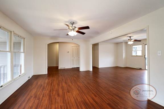 A spacious living area with hardwood floors, ceiling fan, and arch way.