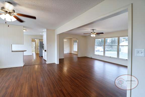 A spacious living area with dividing arch, hardwood floors, and ceiling fans.