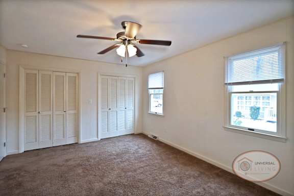A bedroom with carpet, multiple closets, and a ceiling fan.