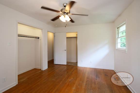 A bedroom with two closets, hardwood floors, and ceiling fan.