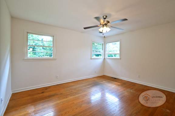 A bedroom with hardwood floors, several windows, and a ceiling fan.