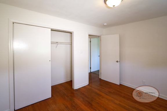 A bedroom with hardwood floors, closet with sliding door, and white walls.