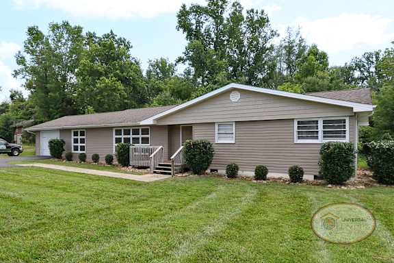 A grey house with attached garage in front of lush green trees.