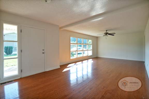 The living room with harwood floors, a ceiling fan, and very large decorative windows and plenty of natural light.