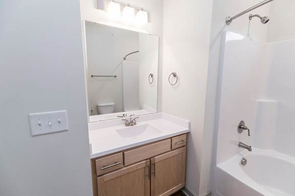 A white bathroom with a sink, mirror, and bathtub at 1701 North Apartment Homes Apartments, Chapel Hill, North Carolina