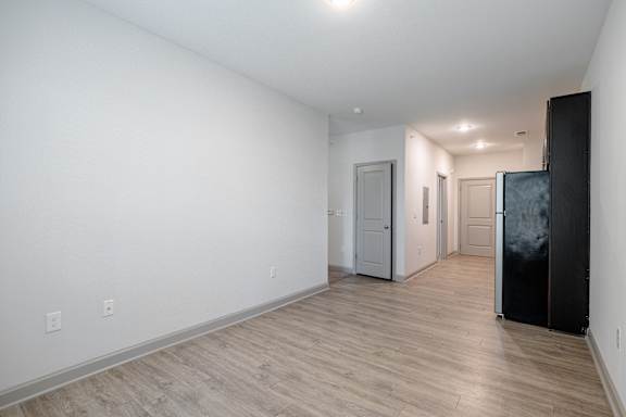A black refrigerator is in the corner of a room with white walls and wood flooring at 1701 North Apartment Homes Apartments, Chapel Hill, NC, 27514