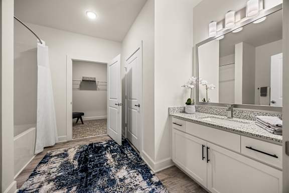 A bathroom with a rug on the floor and a mirror above the sink.