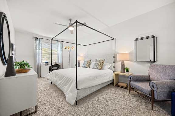 A bedroom with a four poster bed, a chair, and a mirror.
