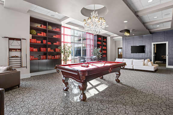 A pool table is in the middle of a room with a grey carpet at Sophia Square Apartments, Carmel