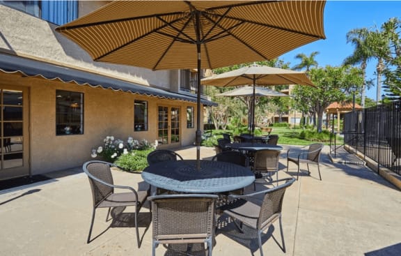 a patio with tables and umbrellas in front of a building at Huntington Terrace North Senior, California, 92648