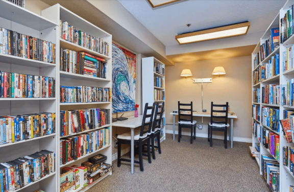 a library with bookshelves and a table with chairs at Huntington Terrace North Senior, Huntington Beach, CA 92648