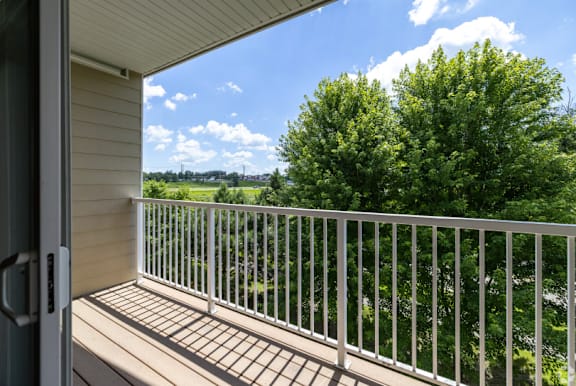 A balcony with a white railing and a view of trees and a blue sky.
