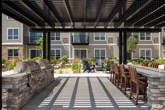 A patio with wooden chairs and tables is surrounded by a brick wall and a building with balconies.